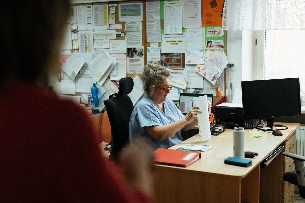 Mitarbeiterin in Praxiskleidung arbeitet an einem Büroschreibtisch mit Unterlagen und Bildschirm
